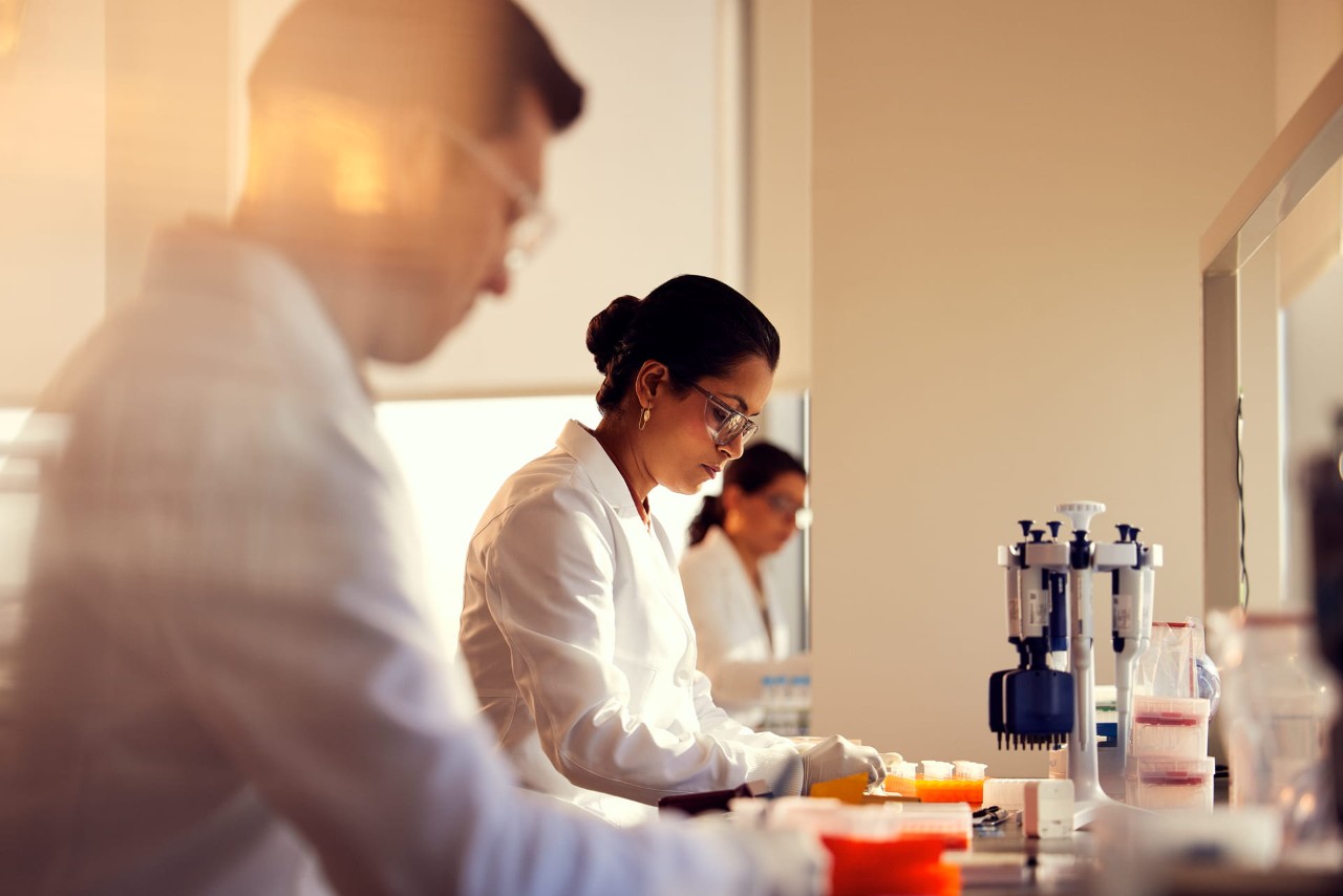Three scientists, side view, interacting at lab bench in wet lab